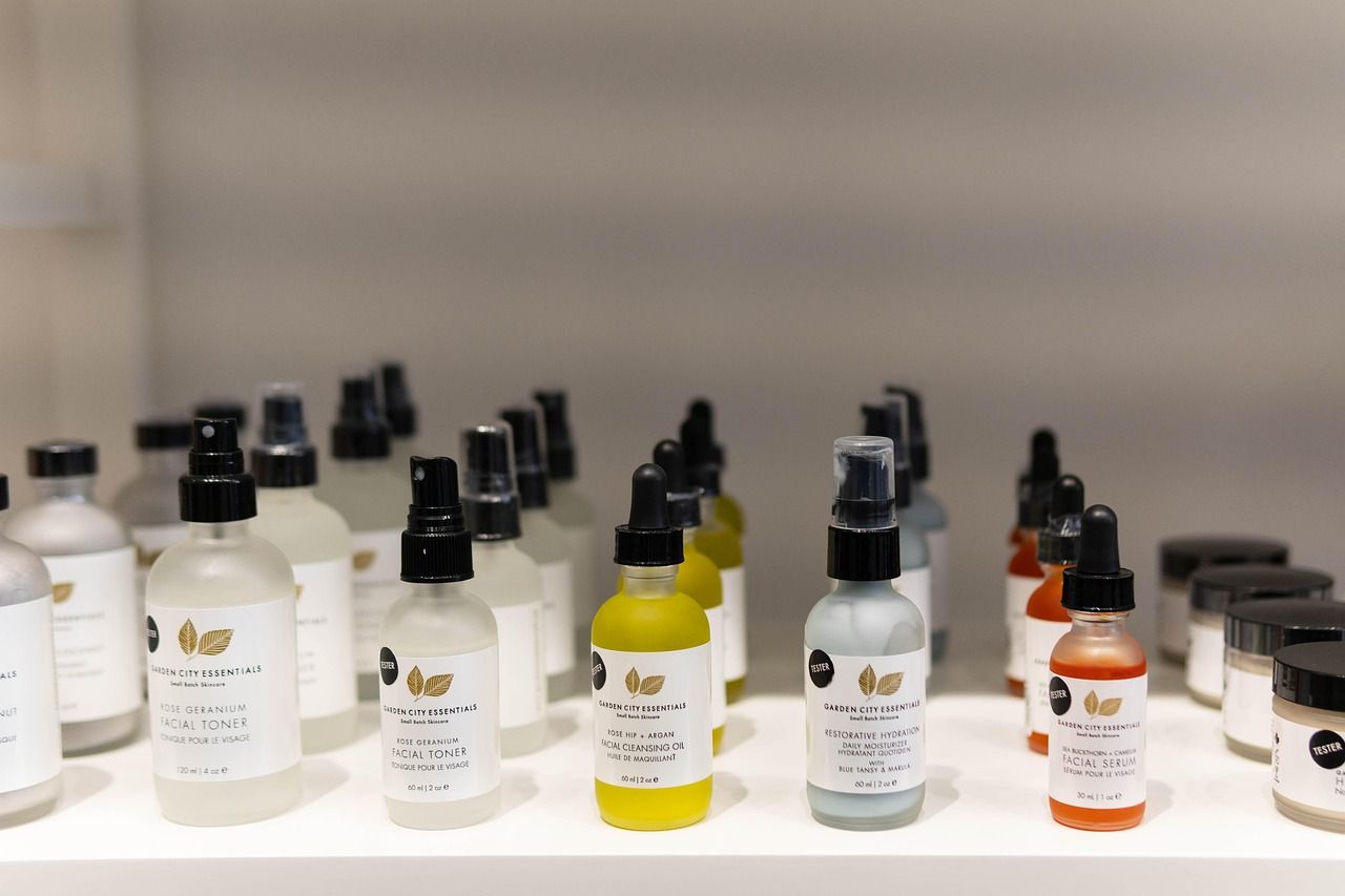 A shelf displays various skincare bottles with dropper tops and labels. The products include facial toners and serums in clear, yellows, and orange hues.