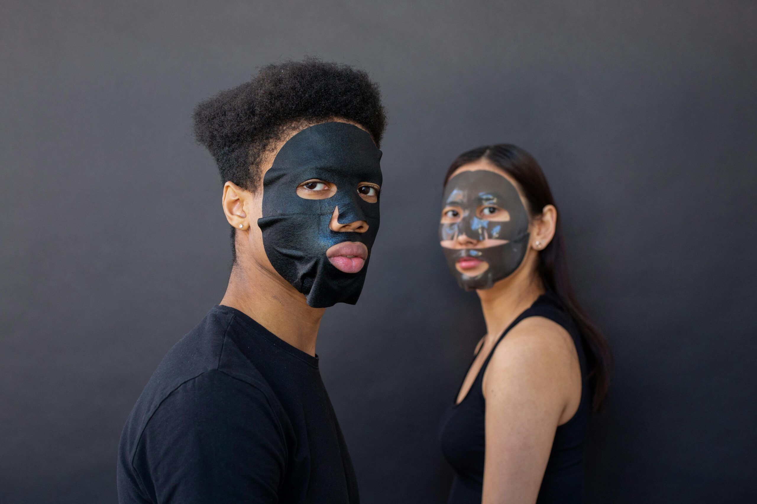 A diverse couple with black facial masks in a studio setting, promoting skincare.